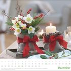 Kalender mit Dezember am unteren Rand. Blumengesteck und Kerze, beide mit roten Schleifen dekoriert.