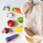 Holzgemüse (Karotte, Tomate, Aubergine) und ein flauschiger Rucksack mit Bärenohren auf hellem Untergrund.