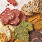 Verschiedene Brotsorten in bunten Farben wie Rot, Grün und Gelb, jeweils in feine Scheiben geschnitten.
