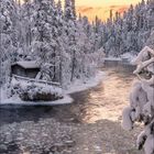 Kalenderseite für Dezember 2027. Winterlandschaft: Ein zugefrorener Fluss, schneebedeckte Bäume, Sonnenuntergang in zartem Rosa.