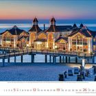 12 2023. Ein beleuchtetes Seebadgebäude auf einer Brücke, umgeben von Wasser und Strandkörben, bei Sonnenuntergang.