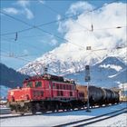 Rote Lokomotive mit der Aufschrift "1020 005", im Hintergrund verschneite Alpengipfel und blauer Himmel.