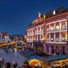 Festlich beleuchtetes Gebäude, verzierte Fenster, Weihnachtsmarktstimmung, viele Menschen, klare blaue Abenddämmerung.