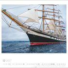 12 2027, ein Segelschiff mit weißen Segeln auf offenem Meer, daneben eine farbige Flagge am Schiffsmast.