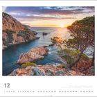 Monat 12, Cala de Roca. Zerklüftete Küstenlandschaft im Sonnenuntergang mit klarem Wasser und Bäumen im Vordergrund.