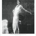 "Josephine Baker" steht unter dem Bild. Eine elegant gekleidete Frau an einem Klavier, lächelnd. Links ein weißes Federkleid.
