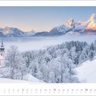 12 2027: Verschneite Landschaft mit Bergpanorama, Kirche im Vordergrund, neblige Täler und sonnenerleuchtete Gipfel.