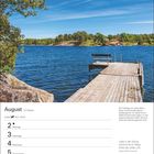 Augustkalender. Ein Steg führt ins blaue Wasser, umgeben von Bäumen und Häuschen, sonniger Himmel.