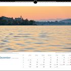 "Dezember" steht in großer Schrift. Eine ruhige Wasseroberfläche bei Sonnenuntergang, im Hintergrund eine silhouettierte Kirche.