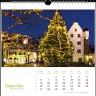 Dezemberkalender: Wochentage und -zahlen. Weihnachtslichter an Bäumen und auf einem großen Weihnachtsbaum vor einem Gebäude.