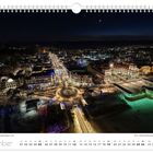 Dezember-Kalender mit nächtlicher Winteraufnahme von Binz, beleuchtete Gebäude und Straßen, darunter ein Kreisverkehr.