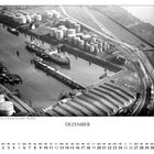 "DEZEMBER" steht groß geschrieben. Eine Luftaufnahme zeigt einen Hafenbereich mit Tankschiffen und vielen Lagertanks.