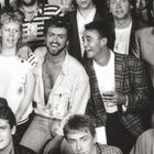 Mehrere Personen lachen und tragen Namensschilder; eine Person hält ein Getränk. Sie scheinen in fröhlicher Stimmung.