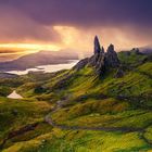 Kein Text zu erwähnen. Eine dramatische Landschaft mit grünen Hügeln, Seen und markanten Felsformationen bei Sonnenuntergang.