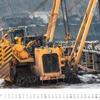 Der Text am unteren Rand lautet "DEZEMBER" und zeigt einen Kalender von Mittwoch bis Samstag. Eine gelbe Baumaschine bewegt sich durch schlammiges Gelände.