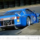 Text: "G.Sport GS G. Schneider", "Shell", "Pirelli". Rennwagen auf einer Strecke, blaue Farbe, Kalender unten: "DEZEMBER".