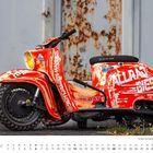 „Juni.“ Ein rot-weiß gespritzter Roller mit Texten wie "ALLRAD", vor einer rostigen Wand.
