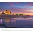 Dezember 2027 | Die Insel Sylt. Kalenderansicht, Abendstimmung am Strand, beleuchtetes Gebäude, bunte Lichter, ruhiges Meer.