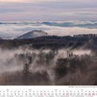 Kalender für Dezember 2027 mit Adventssonntagen und Feiertagen. Nebliger Wald, Hügel im Hintergrund.