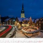 Kalenderseite: Dezember 2027. Winterliche Stadtansicht mit beleuchtetem Adventskranz und Lichterketten.