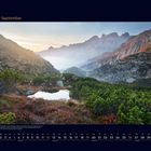 09 September. Berglandschaft mit grünem Tal, Felsen und kleinem Teich im Vordergrund, dahinter Berge im Dunst.