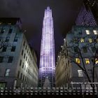 "Weihnachten am Rockefeller Center 12" steht vor einem beleuchteten Hochhaus, flankiert von Gebäuden und einem Weihnachtsbaum.