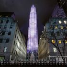 "Weihnachten am Rockefeller Center 12." Hohe Gebäude, ein beleuchteter Baum und Flaggen in einer winterlichen Stadtszene.