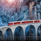 Kalender: Dezember. Schnee bedeckte Bäume, ein roter Zug fährt über eine steinerne Bogenbrücke vor einer Felswand.