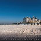 Winter Strand im Ostseebad Sellin (Rügen). Ein Steg führt zu einem Gebäude auf Sand, blauer Himmel darüber. Kalender unten.