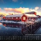 "Rote Fischerhütten (Rorbuer) auf den Lofoten". Es sind schneebedeckte, rote Holzhütten am Wasser unter einem farbigen Himmel.