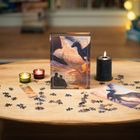 "Fourth Wing" ist in der Mitte auf einer Puzzle-Schachtel zu sehen. Ein Holztisch, Kerzen, Puzzleteile und ein Bild mit Drachen.