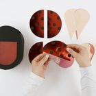 Rote, schwarze, gepunktete Bastelteile in Form von Halbkreisen und Tropfen. Hände halten einen Halbkreis.