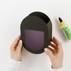 Text: „BASTELKLEBER HOBBY GLUE“. Hände halten einen ovalen schwarzen Karton mit lila Feld, daneben eine Kleberflasche.