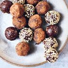 Auf einem rustikalen Teller liegen Schokotrüffel, teils mit Kakaopulver bedeckt, teils mit Sesam bestreut.