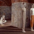 Drei Figuren aus Stein in einer gewölbten Backsteinhalle, zwei stehen nebeneinander, eine kauert im Hintergrund.