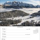 "Zauber der Alpen 2027" steht auf einem Kalender. Er zeigt eine Hütte in einer grünen Berglandschaft mit See bei Sonnenuntergang.