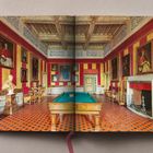 Ein opulenter Raum mit roten Wänden, gemustertem Boden, Porträts, Mobiliar und einem Billardtisch in der Mitte.