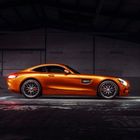 "V8 BITURBO" auf der Seitenöffnung eines orangen Sportwagens, der in einem dunklen Raum parkt.