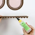 Flasche mit grünem Etikett: "BASTELKLEBER, HOBBY GLUE, COLLE À BRICOLAGE, LIIMOTSELIM". Hände halten Pappe, tragen Kleber auf.