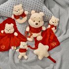 Plüschtiere im Winnie-the-Pooh-Design, einige mit rotem Stoffmantel, auf einer grauen Decke arrangiert.