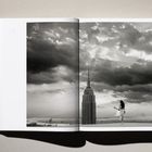Offenes Buch zeigt ein Foto mit Wolken über einer Stadt, ein Wolkenkratzer und eine Person mit Gitarre nahe dem Rand.
