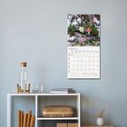 Text: "Januar 2027" mit einem Monatskalender. Winterszene mit Tannenzweigen, Zapfen, rotem Fliegenpilz. Wand und Regal in modernem Raum.