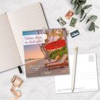 „Schön, dass es dich gibt! 2027“ auf einem Kalender vor Palmen und roten Liegestühlen. Umschlag, Schreibheft, Stifte.