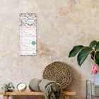 "Wir planen das 2027." Wandkalender mit floralen Mustern, Holztisch mit Pflanze, Uhr und Kissen.
