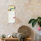 Kalender mit "Einfach planen 2023". Daneben Pflanzen, ein Wecker und ein gefalteter Schal auf einem Holzregal.