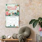 Text: "FAMILIEN PLANER", "Aquarell". Illustration: Personen, Bücherstapel und Sofa. Umgebung: Pflanze, Kissen, Uhr.