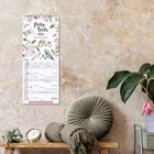 Familienplaner mit der Aufschrift "Pretty Birds 2024". Daneben Sofakissen, eine Pflanze und eine kleine Uhr auf einem Tisch.