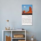 Text "Januar 2027" auf einem Wandkalender mit Landschaftsfoto. Darunter ein Regal mit Wasserflasche und Büchern.