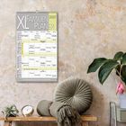 "XL Familien Planer 2027" steht oben auf einem Wandkalender. Darunter ein Tisch mit Kissen, Uhr und Pflanze.