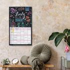 "Lovely chalk timer 2023". Ein Kalender mit Blumenillustrationen an einer Wand. Daneben stehen ein Pflanzenarrangement und ein Kissen.